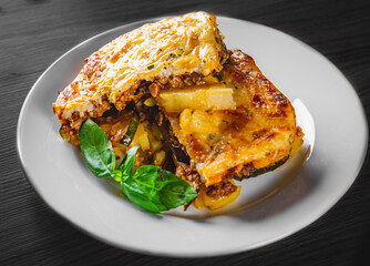 Traditional greek moussaka in white plate on black wooden table background