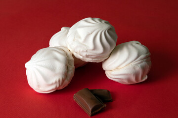 Four white delicate zephyrs and little pieces of chocolate against bright red saturated background