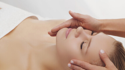 Young, beautiful and healthy woman in massaging salon. Traditional face massage therapy and skin care.