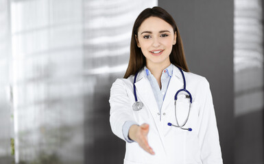 Young woman-doctor is offering her helping hand for shaking hand or saving life. Physician is ready to help patients. Medical help, insurance in health care, best disease treatment and medicine