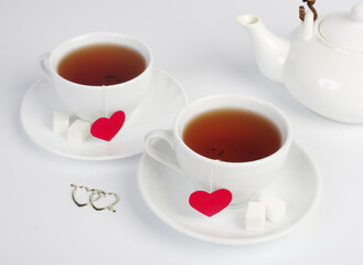 Two white cups of tea with red hearts in the form of labels on a white background.Tea for two.