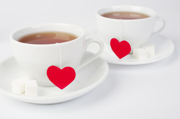 Two white cups of tea with red hearts in the form of labels on a white background.Tea for two.