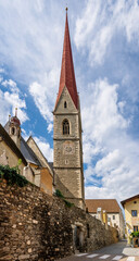 Fototapeta na wymiar The high bell tower of the parish church of Santa Maria Assunta (in German Pfarrkirche Mariä Himmelfahrt) in Silandro, South Tyrol, Italy, under a beautiful sky