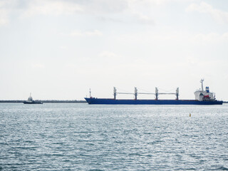 A long blue ferry floats on the sea following a small ship against a cloudy sky