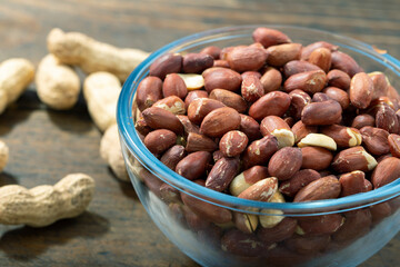Peanuts in their husks in a glass bowl and peanuts in their skins are scattered on the table. Space for text.