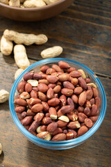 Peanuts in their husks in a glass bowl and peanuts in their skins are scattered on the table. Space for text.