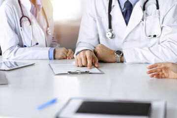 Unknown male doctor listening to his patient woman while sitting in sunny clinic. Medicine concept during Coronavirus pandemic. Covid 2019