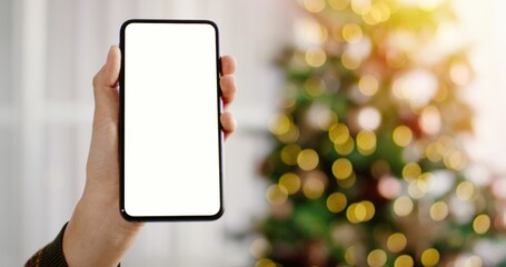 Close up of black smartphone with blank screen in woman hands. Mobile phone with empty screen on background of beautiful christmas tree with lights.