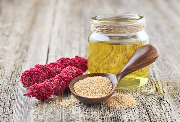Amaranth oil with plant and seeds on wooden background