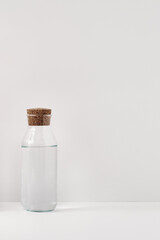 Transparent bottle with water, with a cork stopper on a white background. Minimalism, eco-materials in the interior decor. Copy space, mock up