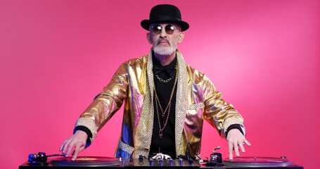 Vintage stylish fancy retired man in hat and sparkling golden coat playing music as DJ on special...