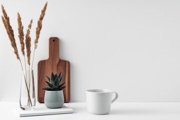 A mug and potted houseplant, a stack of books, a transparent vase and a wooden board. Eco-friendly materials in interior decor, minimalism. Copy space, mock up.