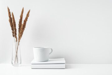 A mug on a stack of books and a transparent vase with dried flowers. Eco-friendly materials in interior decor, minimalism. Copy space, mock up.