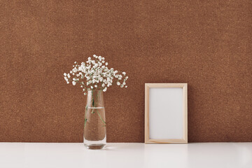 Wooden frame and vase with white flowers, cork background. Mock up, copy space. Folk.