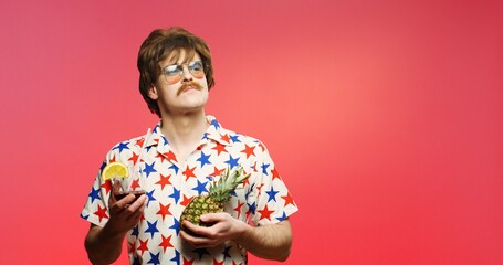 Portrait of joyful male model with glass of drink and pineapple. Funny retro style Caucasian man with mustache drinking cocktail. Vintage guy in shirt with stars over punch pink background wall