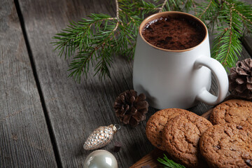 Happy New Year composition. Christmas still life made of fir branches, white cup of cocoa, oatmeal cookies with chocolate and pink toys on a rustic black wooden background.