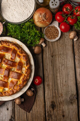 Ruddy meat pie on wooden table with variety of ingredients background. Concept of cooking process. Backstage of preparing tasty meal. View from above. Flat lay. Recipe book. Space for text. Vertical