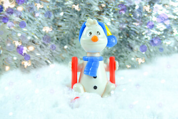   toy funny snowman by ski in snow on  festive blurred background . Festive design. Christmas concept