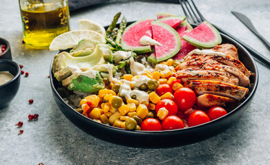 Buddha bowl with brown rice, grilled chicken breast, avocado, tomato, peas, corn, watermelon radish, asparagus