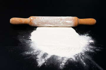 In the center of the screen on the table is a hill of white flour. On top located kitchen rolling...