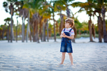 Adorable active little kid boy having fun on Miami beach, Key Biscayne. Happy cute child relaxing, playing with sand and enjoying sunny warm day near palms and ocean