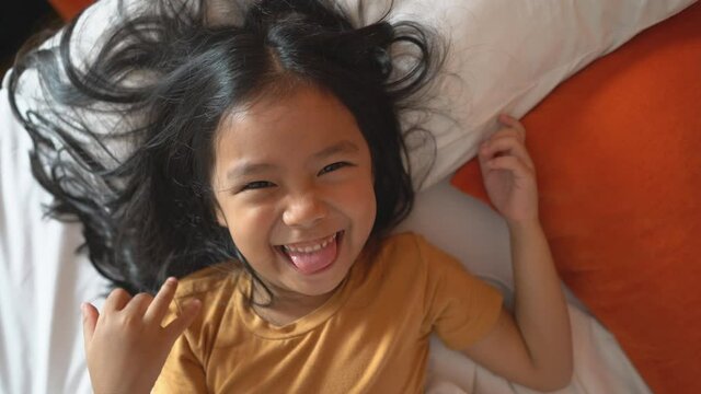 Asian child cheerful or kid girl sleeping and wake up with play peekaboo in blanket by father or parents for relax on white bed in bedroom and smile laugh for enjoy happy fun in morning on holiday 4K