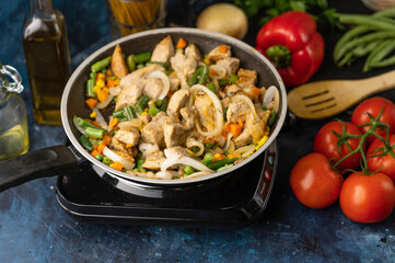 Pan with fragrant frying meat on marble dark blue table with variety of ingredients background. Backstage of cooking spaghetti pasta. Concept of cooking process. Cookbook design.