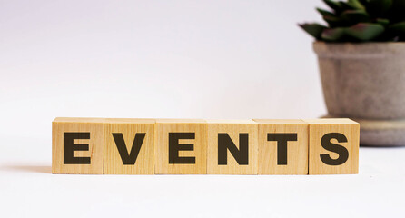 The word EVENTS on wooden cubes on a light background near a flower in a pot. Defocus