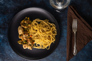 Plate with appetizing spaghetti pasta with fragrant frying chicken on marble dark blue background. Traditional italian dish. View from above.