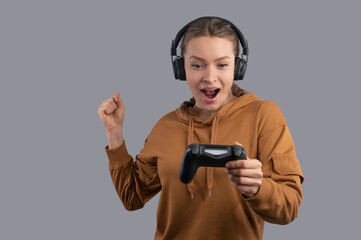 Surprised gamer woman in headphone with pigtails using joystick on grey background. Concept of playing video games.