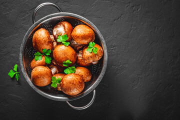Fresh raw mushrooms champignons in stainless steel colander on Dark grey black slate background