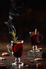 The traditional winter drink is mulled wine in a glass glass. Hot wine with spices and rosemary on a dark background