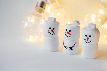 team of marshmallow snowmen on a beige background in the lighting of a garland