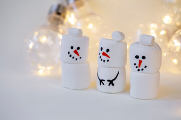 team of marshmallow snowmen on a beige background in the lighting of a garland