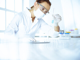 Female laboratory assistant analyzing test tube with blue liquid. Medicine, health care and researching concept