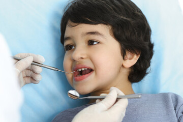 Cute arab boy sitting at dental chair with open mouth during oral checking up with doctor. Visiting dentist office. Stomatology concept