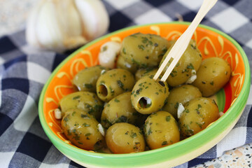 Ripe olives with garlic and parsley in colorful clay bowl, closeup
