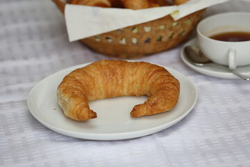 A Bamberg croissant on a plate beside a cup of coffee and a bread basket on a table in Germany.