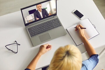 Senior woman taking notes while having video call with colleague or listening to business lecturer