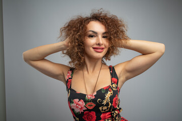 beautiful curly red-haired girl in a black dress with bright flowers on a gray background in a photo studio