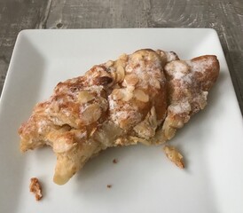 Bitten almond croissant on a white plate against a wooden background