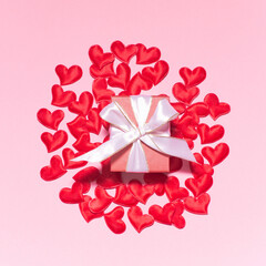 Red hearts and gift box with write bow and ribbon on pink background. Valentine's day composition. Top View, flatly, center composition.