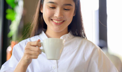 Asian Woman drinking coffee  enjoying her morning coffee. Smiling happy multiracial female Asian Chinese
