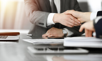 Unknown businessman shaking hands with his colleague or partner above the desk in sunny office, close-up