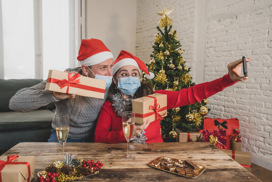 Happy couple with face mask and smart phone on video call celebrating virtual christmas