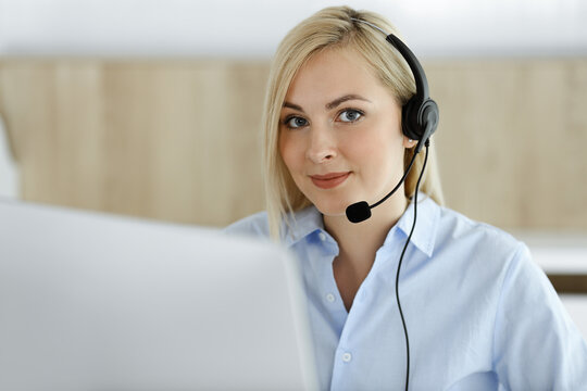 Blonde business woman sitting and communicated by headset in call center office. Concept of telesales business or home office occupation