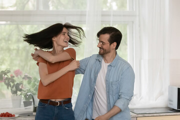 Happy laughing carefree young family couple twisting dancing to favorite energetic music, enjoying romantic dating time together at home or involved in domestic hobby activity, weekend pastime concept