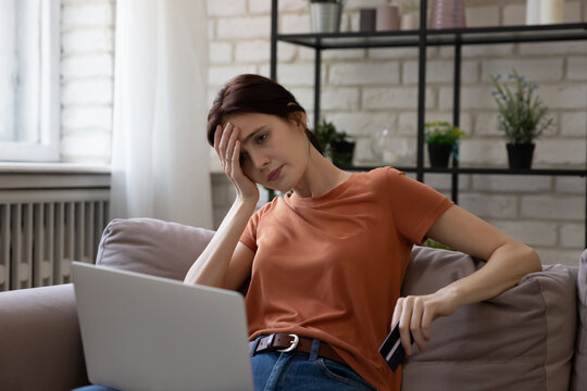 Unhappy young caucasian woman looking at computer screen, feeling stressed entering wrong payment information from credit card, having lack of money, financial problems or hacked bank account.
