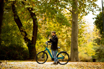 Fototapeta premium Handsome young man with electric bicycle in the autumn park