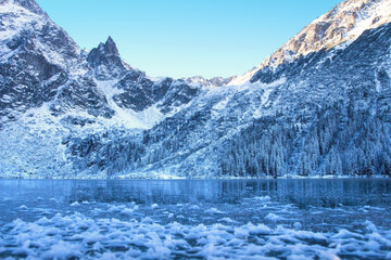 Fototapeta na wymiar Ice winter mountain lake. Amazing frozen rocky mountains on the lakeshore. Winter background. Winter nature.